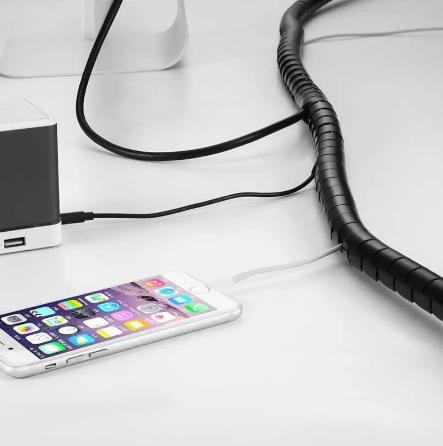 Organizador de cabos em espiral preto agrupando vários fios na mesa, com saída lateral para o cabo do carregador do celular, mantendo o visual clean